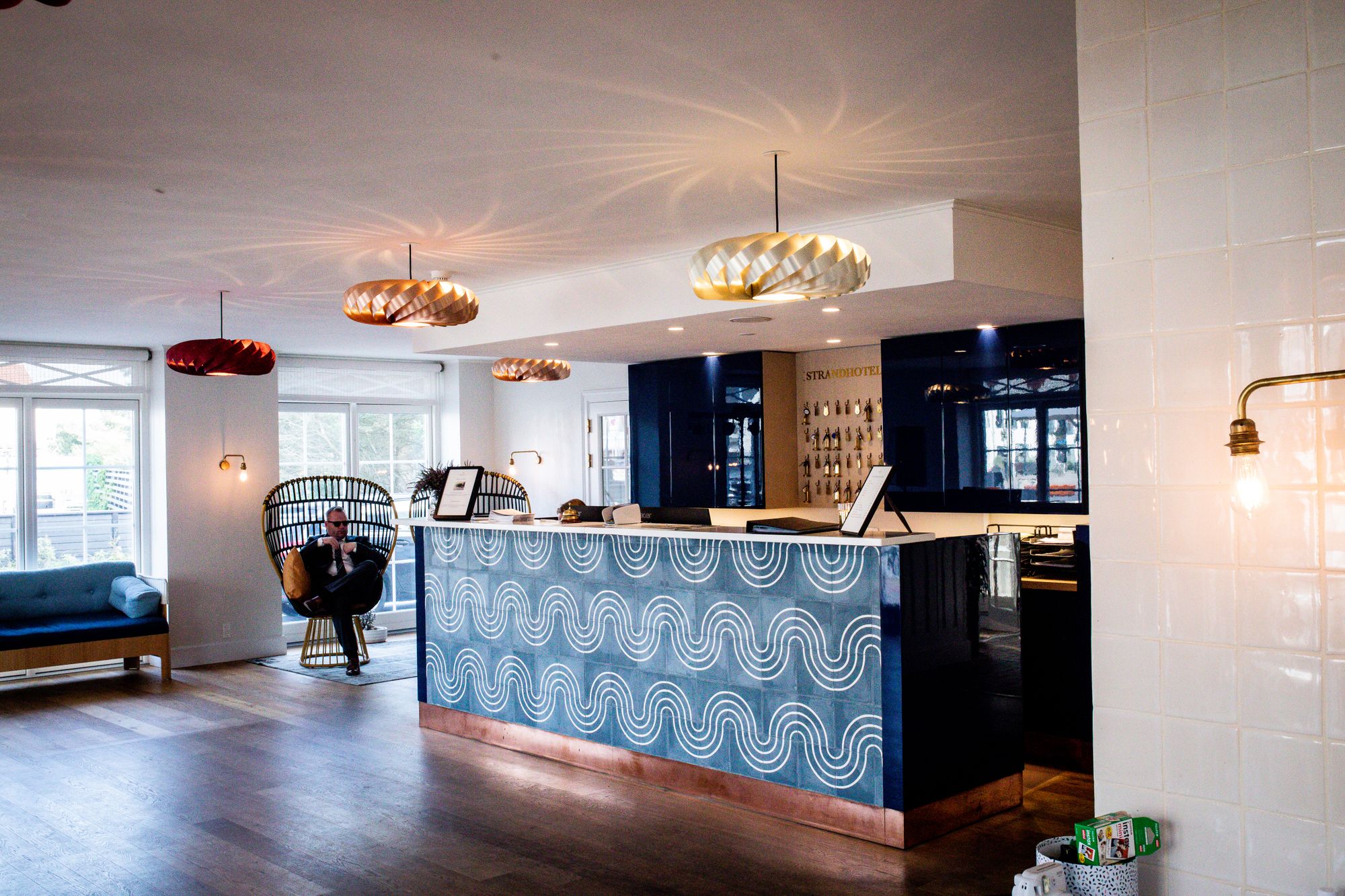 Blue patterned reception desk beneath sculptural pendant lights in a bright hotel lobby.